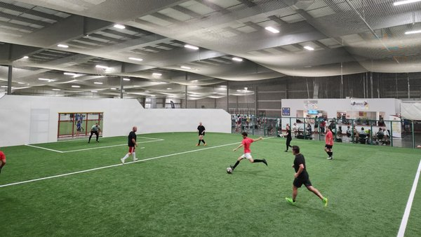 Players competing in an indoor 6v6 soccer game on green turf with a goal and netting